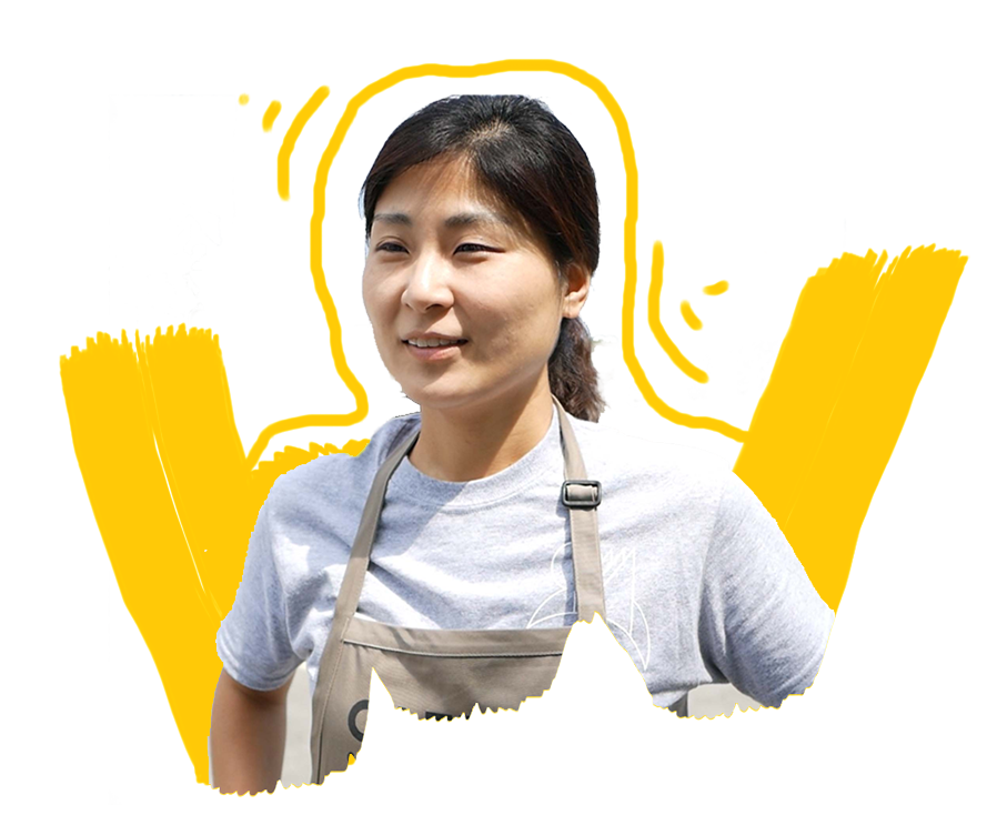 A smiling Korean woman wearing a CAFE branded apron.