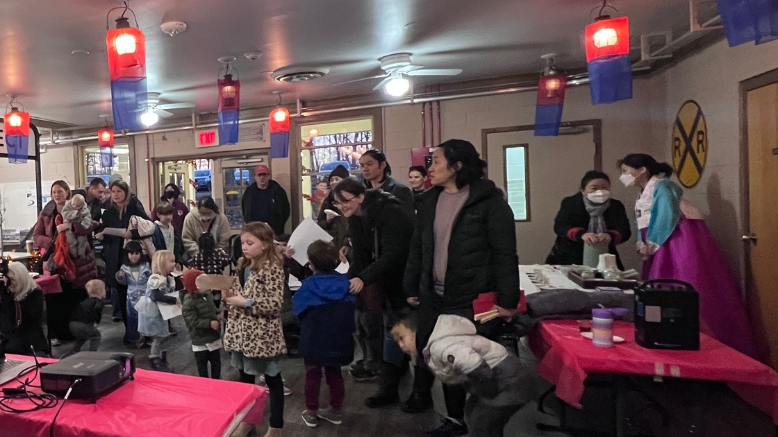 A cafe full of Asian decorations with hanging paper lamps, a woman wearing a hanbok, and children exploring various booths.