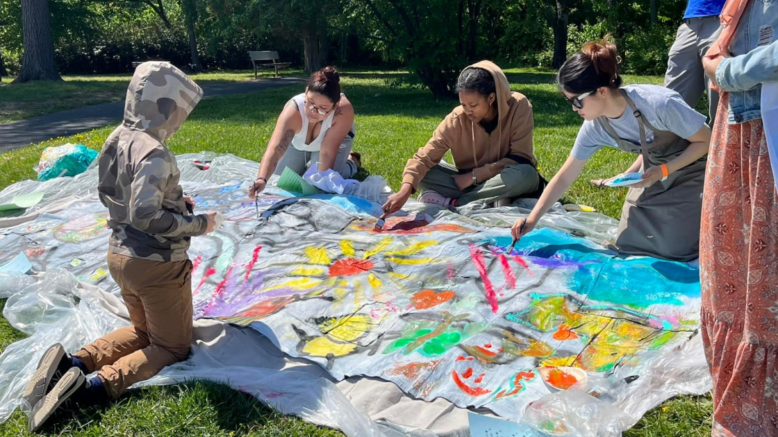 Several community artists kneeling down to paint on a canvas made of denim jeans.